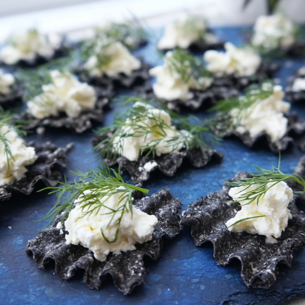 The Stormy Sea appetizer features wavy black crackers topped with creamy goat cheese “whitecaps” on dark slate.