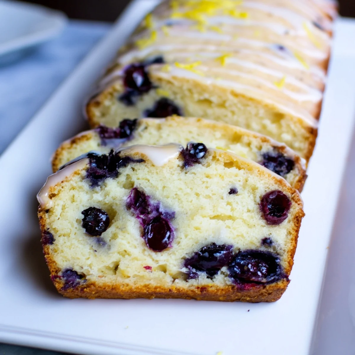 A slice of Lemon Blueberry Yogurt Loaf showcasing fluffy texture, blueberries, and drizzle.