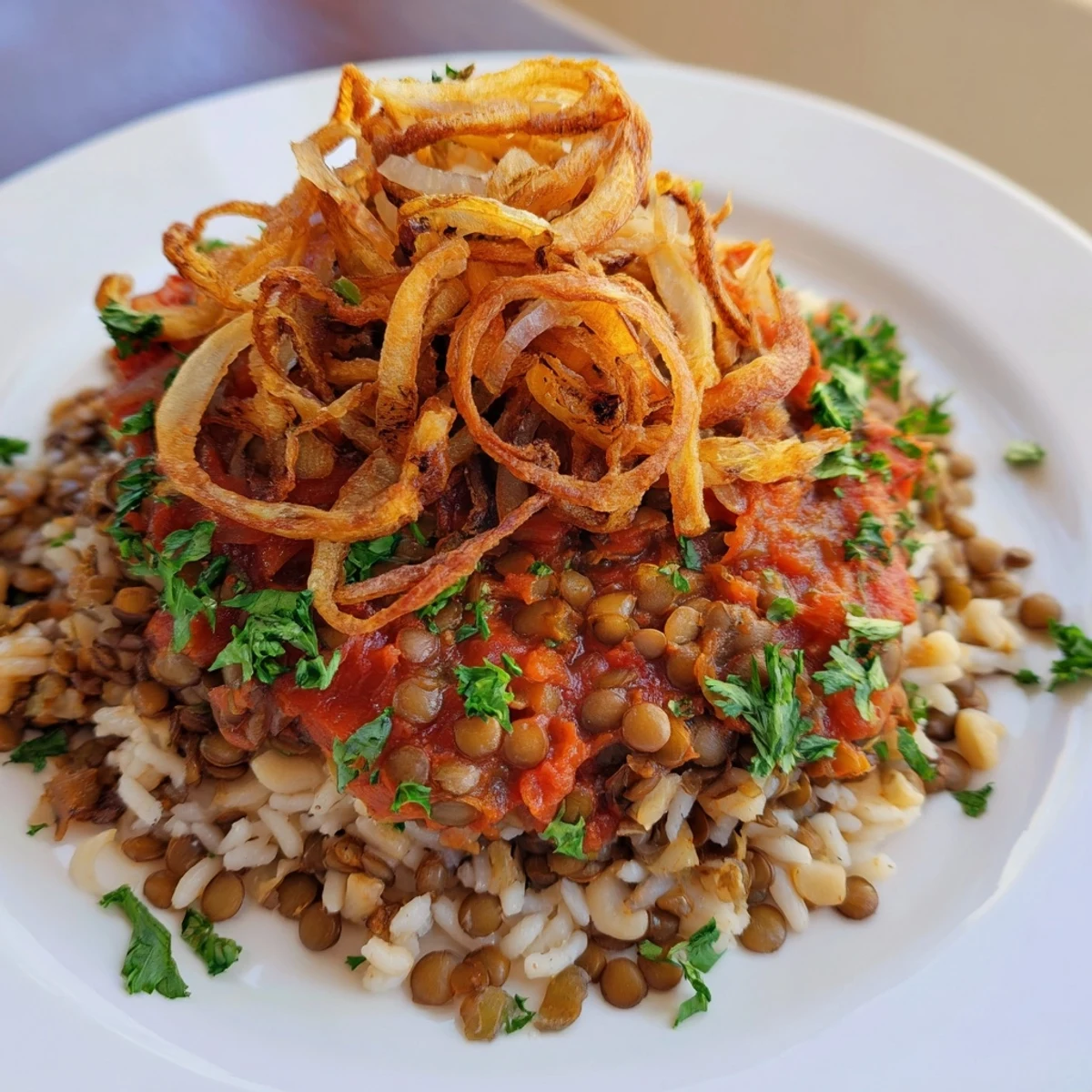 A close-up of a layered serving of Egyptian Koshari, with vibrant red tomato sauce.