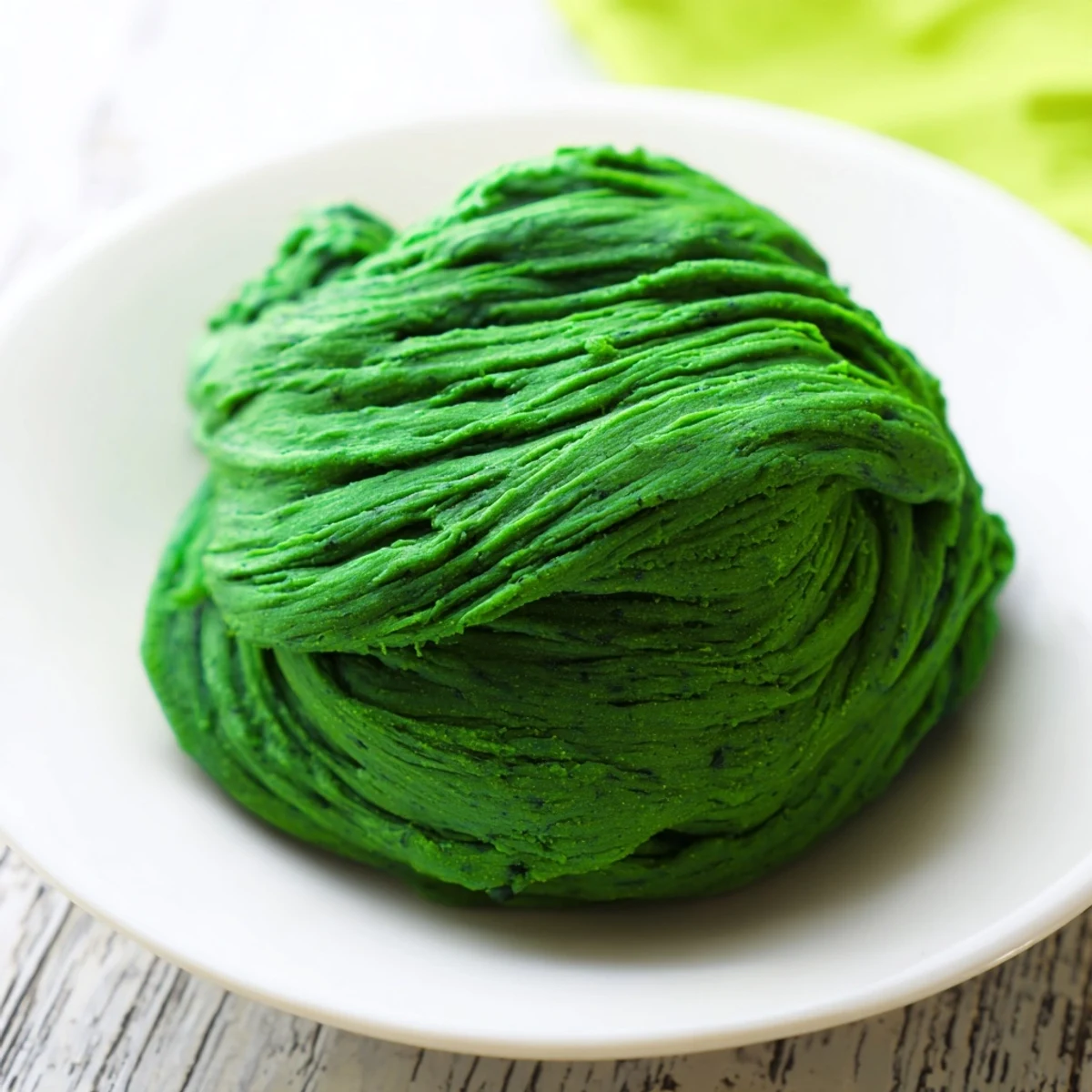 Fresh, vibrant green spinach pasta dough is kneaded smooth on a floured wooden board before resting.  