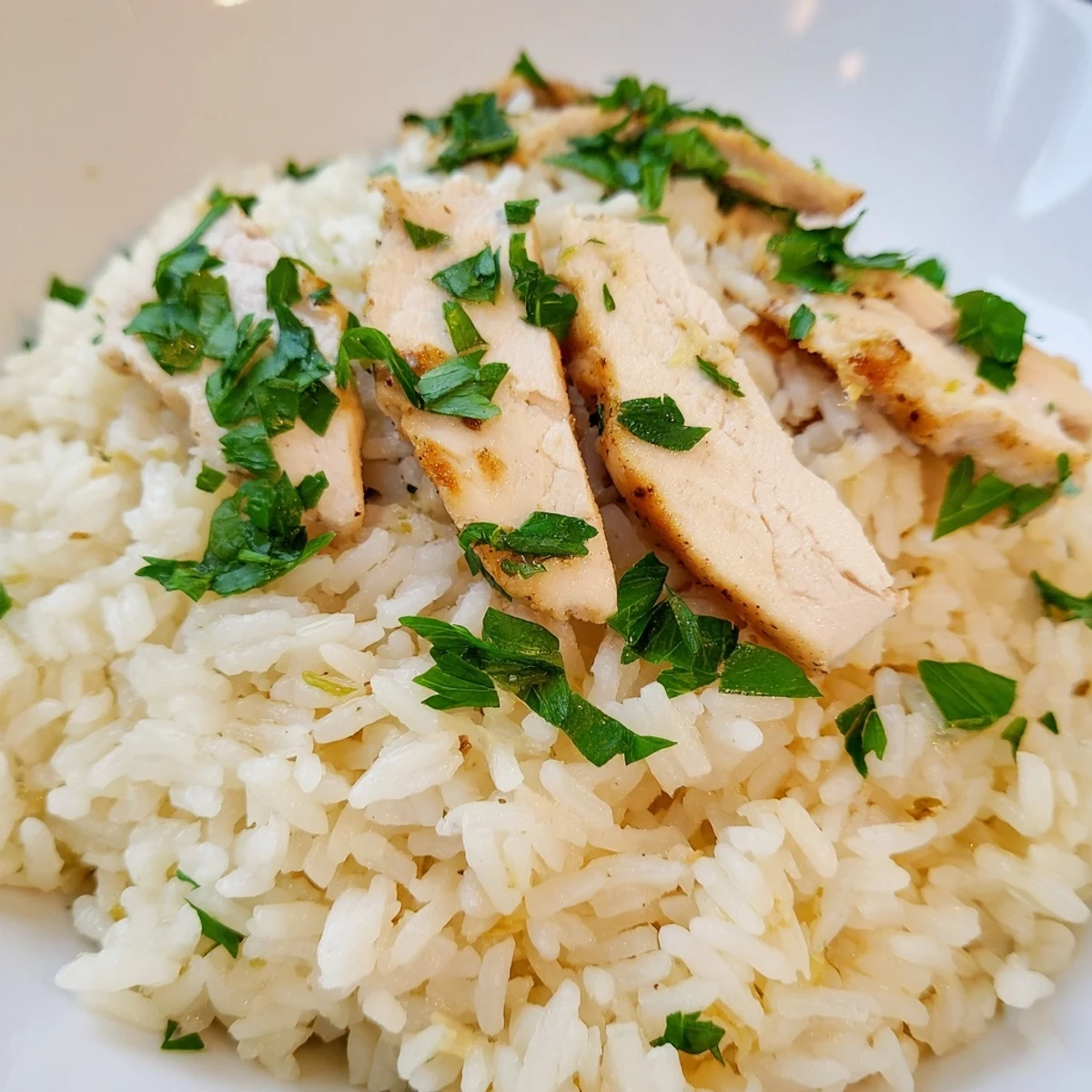 Steaming bowl of garlic butter rice with tender grilled chicken, brightened with a wedge of lemon for serving.