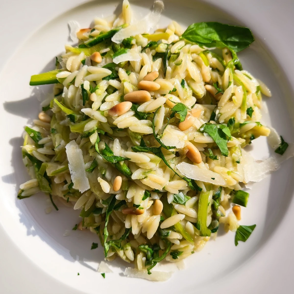 A vibrant bowl of Asparagus Lemon Orzo Salad topped with toasted pine nuts and freshly shaved Parmesan, perfect for summer picnics.