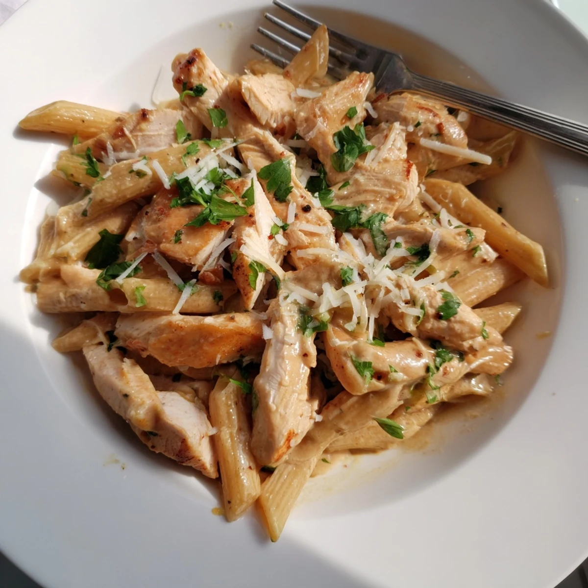 Freshly sliced seared chicken breast resting atop a creamy honey chipotle sauce coating penne pasta, garnished with vibrant cilantro.