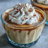 Creamy Hojicha Pudding infused with roasted green tea, garnished with whipped cream and delicate tea leaves, on a rustic wooden table for a cozy treat.