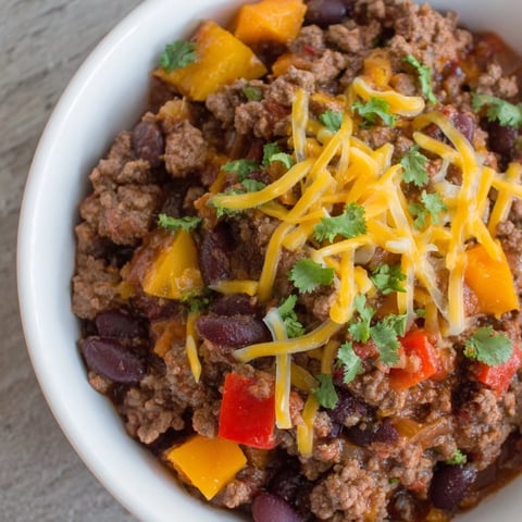 A steaming bowl of simple weeknight chili topped with cheddar cheese and sour cream.