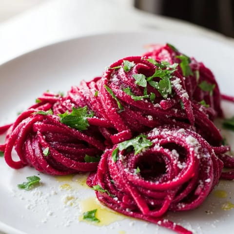 Tender roasted beet noodles tossed with olive oil, fresh basil, and shaved Parmesan on a rustic white plate.
