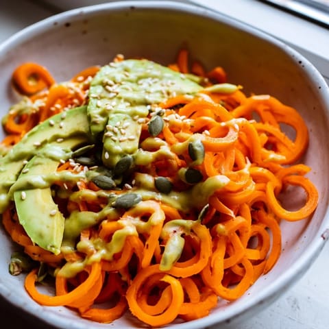 Creamy tahini-lime dressing drizzled over vibrant spiralized carrot noodles, crisp veggies, and sliced avocado in a beautiful bowl.
