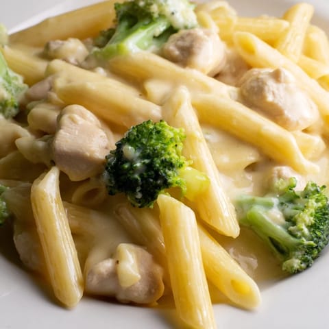 Steaming bowl of homemade Chicken Broccoli Cheddar Pasta, garnished with fresh parsley, served alongside a crisp green salad for a comforting family dinner.