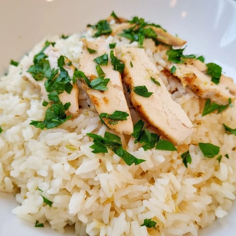 Steaming bowl of garlic butter rice with tender grilled chicken, brightened with a wedge of lemon for serving.