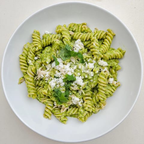 Creamy Cilantro Lime Chicken Pasta with rotini, shredded chicken, and a vibrant green yogurt sauce, garnished with crumbled cotija cheese and fresh lime wedges.  