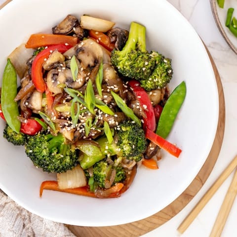 A vibrant plate of Ginger Stir-Fried Vegetables garnished with green onions and toasted sesame seeds, served over fluffy jasmine rice.  