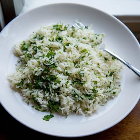 A close-up of fluffy Cilantro Lime Rice garnished with fresh cilantro, lime zest, and a lime wedge.
