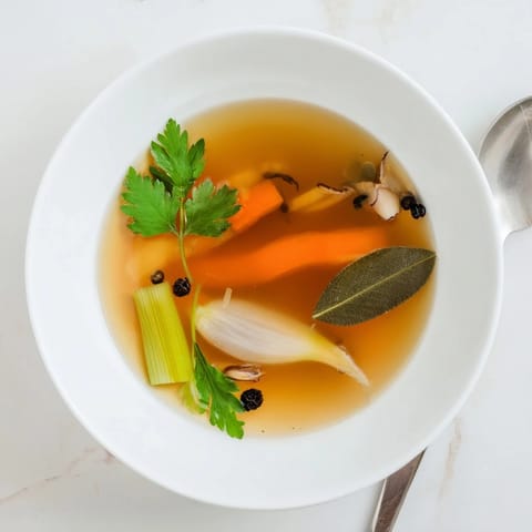 Vegetable Broth From Scraps being strained through a fine-mesh sieve into a glass bowl, showcasing the clear, golden liquid.