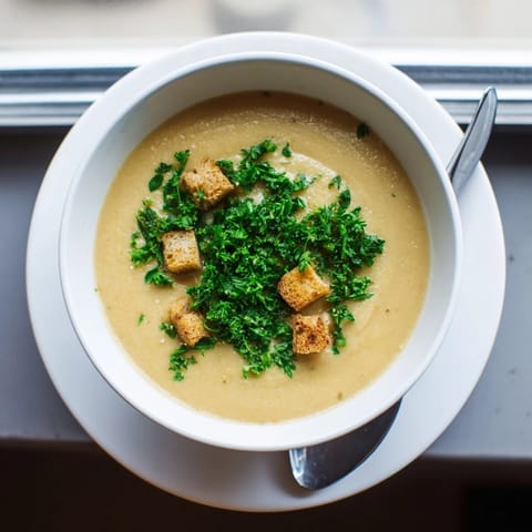 Hearty roasted garlic soup served in a white ceramic bowl, with a side of crusty bread for dipping.