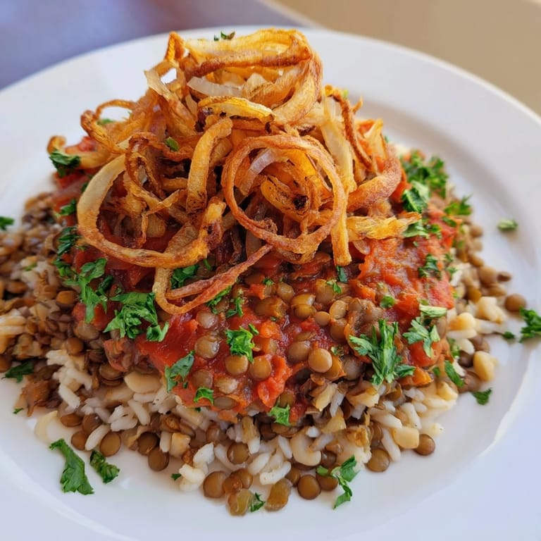 A close-up of a layered serving of Egyptian Koshari, with vibrant red tomato sauce.