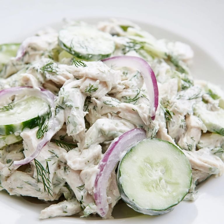 A top-down view of Creamy Cucumber Chicken Salad featuring Greek yogurt dressing, cucumbers, and shredded chicken on a wooden board.