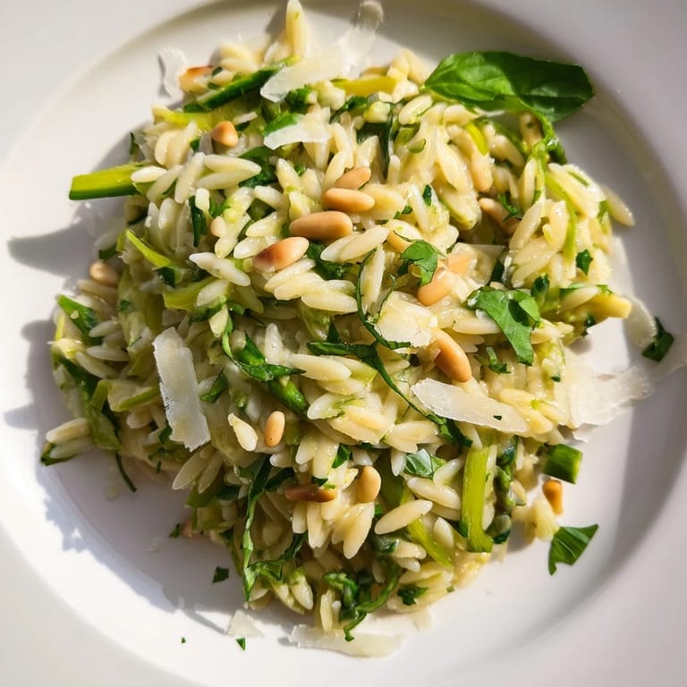 A vibrant bowl of Asparagus Lemon Orzo Salad topped with toasted pine nuts and freshly shaved Parmesan, perfect for summer picnics.